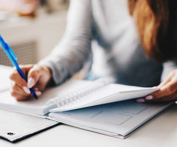 A woman writing in her coaching and consulting notebook wik with a blue pen