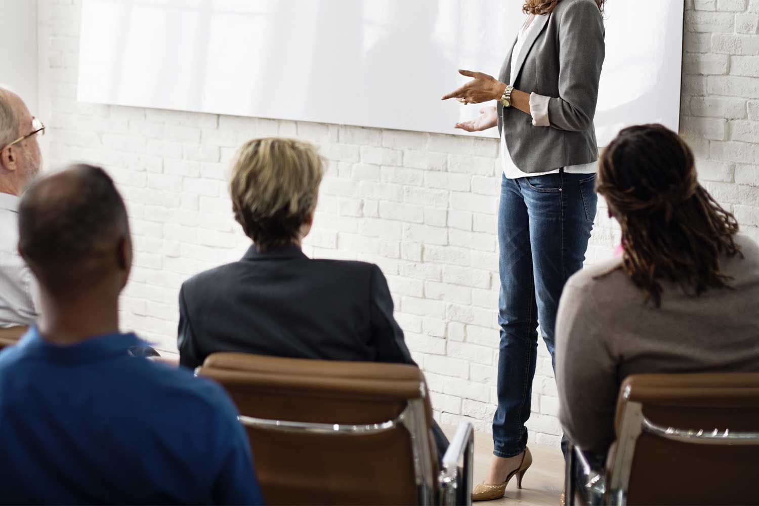 A woman in blue jeans and a gray blazer providing coaching and consulting services to a small team