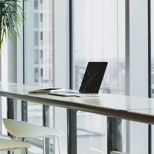 An open laptop on a metal table near a floor to ceiling window during a business consulting session